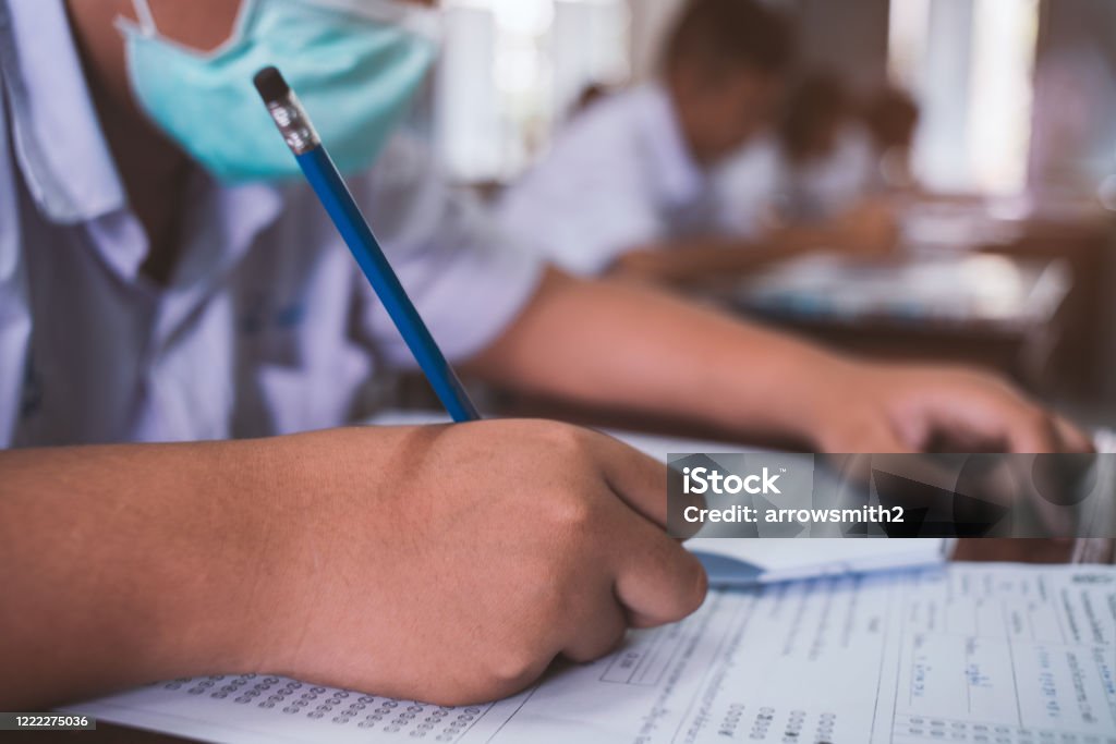 Students wearing mask for protect corona virus or covid-19 and doing exam in classroom with stress. Education Stock Photo