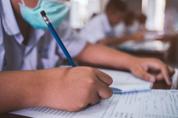 Students wearing mask for protect corona virus or covid-19 and doing exam in classroom with stress. stock photo
