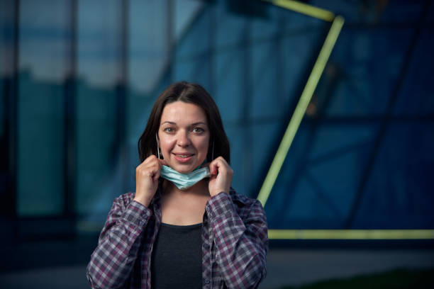 Happy woman takes off protective medical mask outdoors against modern city background. Pandemic Covid-19 is over. Young happy woman takes off protective medical mask outdoors against modern city background. Pandemic Covid-19 is over concept. happy end stock pictures, royalty-free photos & images