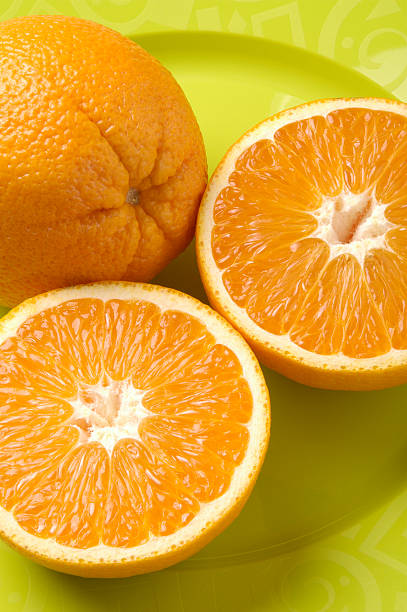 istock One whole orange and one cut in half on a yellow plate. 122227522