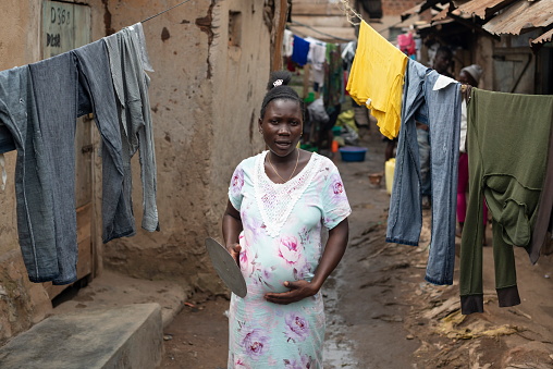 Kampala, Uganda - January 26th, 2020: Unidentified pregnant woman passes by hanging clothes in Katanga slum, Kampala, Uganda. Local people have to stay here without proper health care for women and kids.