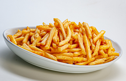 Closeup of hands taking french fries from the plate. Fried foods are cooked in oil at extremely high temperatures, they are likely to contain trans fats which associated with an increased risk of many diseases, including heart disease, cancer, diabetes and obesity.