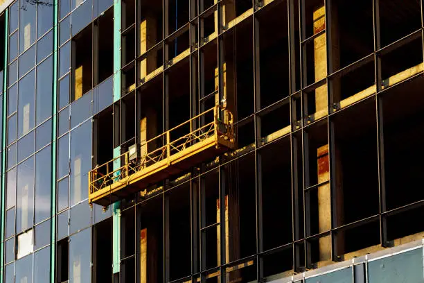 Photo of Suspended construction craddle near wall of hightower building with ventilated facade on construction site. Engineering urban background