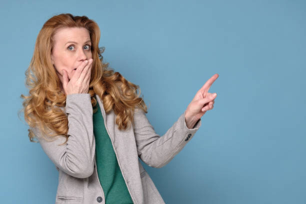 istock woman pointing at copy space aside, surprised middle aged lady on blue wall. 1222281690