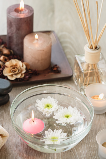 High angle view of decorative aromatic candle and flowers floating on a bwol of water  with more brown candles and aroma diffuser bottle behind for a relaxing massage therapy with volcanic stones in a spa center.