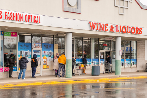 Customers, some practicing social distancing, wait on line to enter a liquor store in Shirley, New York.