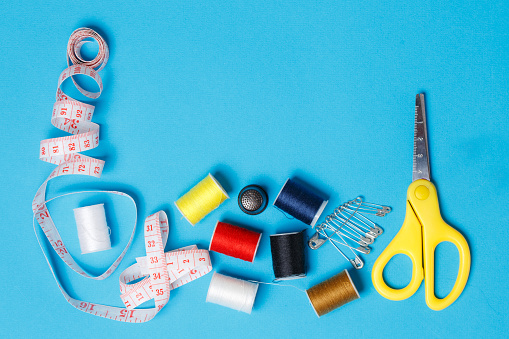 Sewing Accessories Flatlay on Neutral Background. Top View of Yellow Scissors, Spools of Colorful Thread, Bobbin, Pins and Measuring Tape for Tailor. Supplies for Seamstress Workplace.