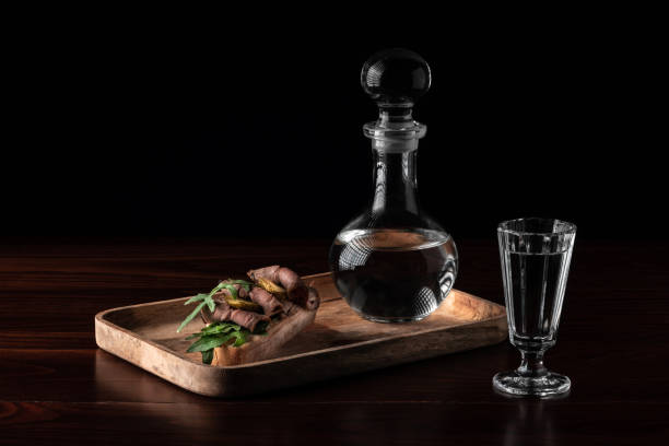 decantador de cristal ou carafe com um copo cheio de vodca e saboroso aperitivo bruschetta com bacon e picles em tábua de madeira, conceito de bebida alcoólica com espaço de cópia - decanter crystal carafe glass - fotografias e filmes do acervo