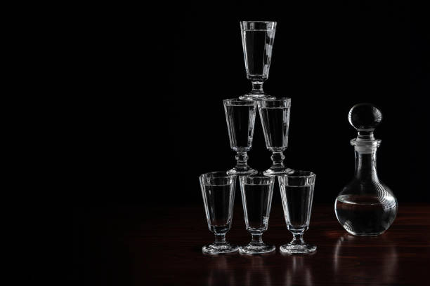 crystal decanter or carafe of vodka and glasses pyramid tower on wooden table in restaurant, black background with copy space - decanter crystal carafe glass imagens e fotografias de stock