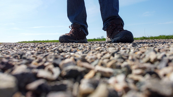 Legs of a man in walking boots stand on a gravel road