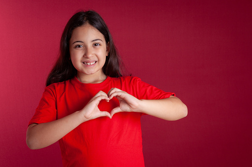 happy child making little heart with his hands on red background.