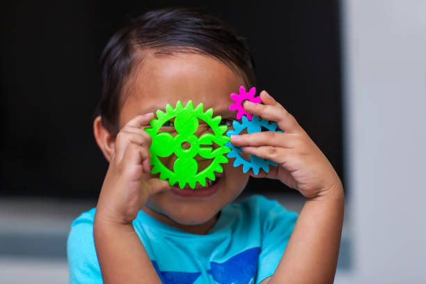 a hispanic boy having fun as he holds a gear set and learns about engineering in a exploratory problem solving environment. - preschooler child playing latin american and hispanic ethnicity imagens e fotografias de stock