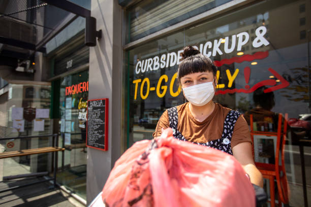 istock Masked Restauranteur During Covid-19 Lockdown Holding Out Bagged Order to Camera 1222296710