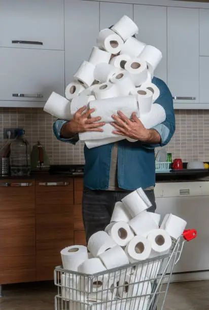 Mature man holding lots of toilet paper rolls in kitchen
