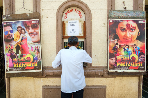 Mumbai, India - May 10, 2016: A man buys movie tickets at the box office outside with Indian movie posters on each side.