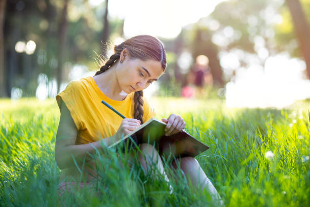 une jeune fille écrivant quelque chose dans le cahier dans le parc - writing diary nature ideas photos et images de collection