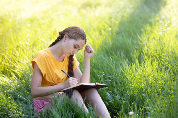 istock a young girl writing something in the notebook in the park 1222323663