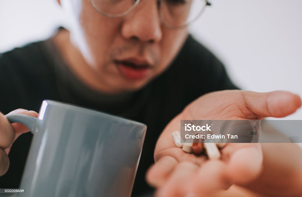 seorang pria dewasa tengah Asia Cina dengan gejala penyakit flu mengambil obat yang berfokus pada pil obat palem tangan - Bebas Royalti Bagian tubuh manusia Foto Stok