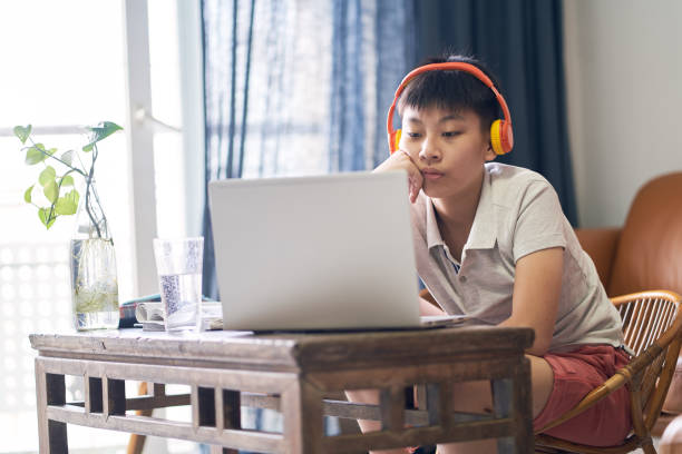 Asian teenage boy studying at home wearing headset stock photo