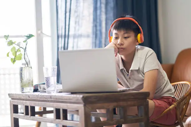 Photo of Asian teenage boy studying at home wearing headset