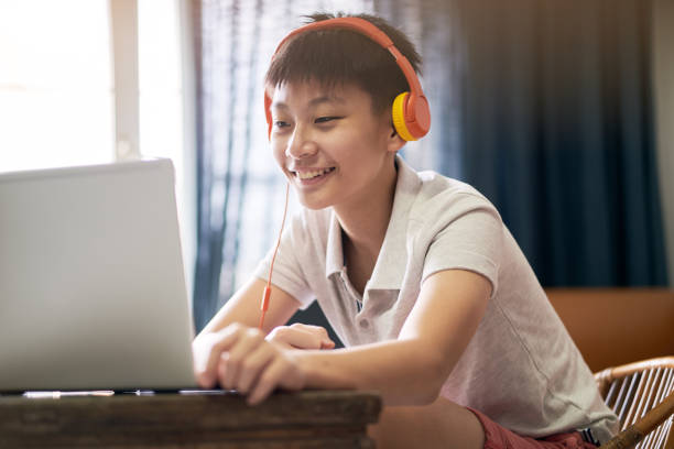 Asian teenage boy taking online lessons at home wearing headset stock photo
