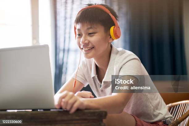 Asian Teenage Boy Taking Online Lessons At Home Wearing Headset Stock Photo - Download Image Now