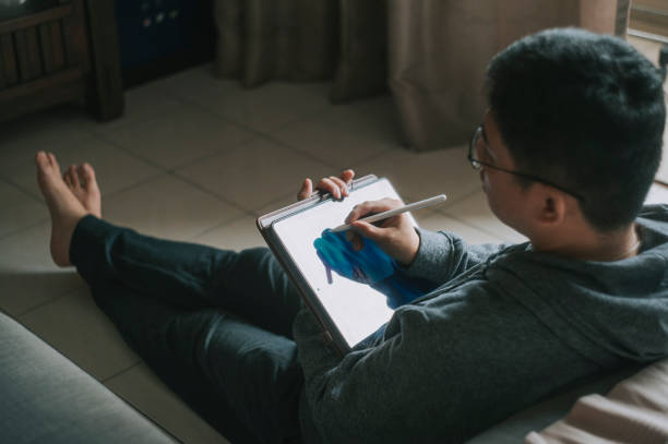 un cinese asiatico mid adult man a casa utilizzando tablet digitale per drraw - tavoletta grafica illustrazioni foto e immagini stock