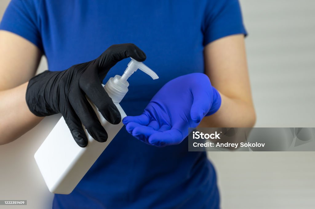 Las manos en guantes quirúrgicos usan antiséptico en un frasco con un dispensador - Foto de stock de Ajustar libre de derechos
