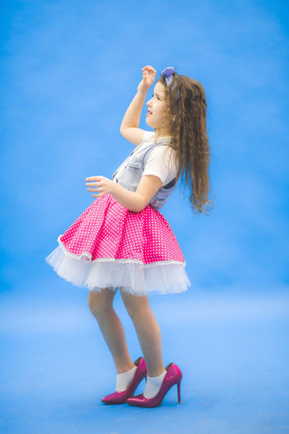 Little girl looking somewhere in the studio. Blue background.