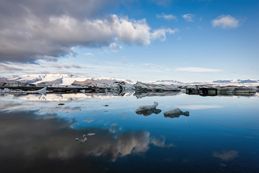 Moody sunrise at Jokulsarlon Lagoon in late summer. Icebergs drifting in the early morning sun from the Vatnajokull Glacier over the lagoon into the North Atlantic Ocean. Long time Exposure. Symmetric relfections in the lagoon water. Jokulsarlon, Iceland, Northern Europe.