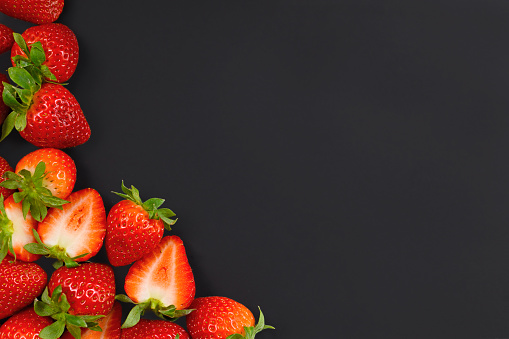 Strawberry background with whole and cut open berry fruits on left and lower side of black blank copy space to right side.