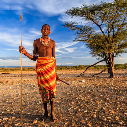 African warrior from Samburu tribe standing on savanna and holding a spear, central Kenya. Samburu tribe is one of the biggest tribes of north-central Kenya, and they are related to the Maasai.