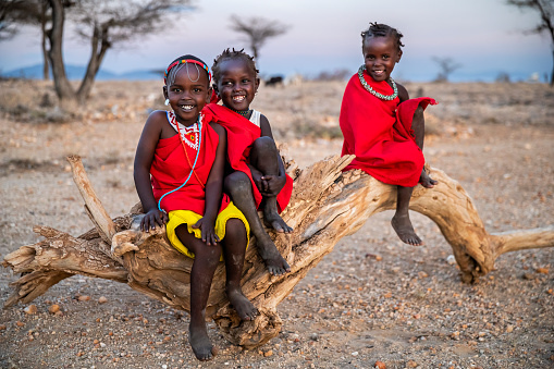 Three happy African little girls from Samburu tribe sitting on tree trunk, Kenya, Africa. Samburu tribe is north-central Kenya, and they are related to  the Maasai.