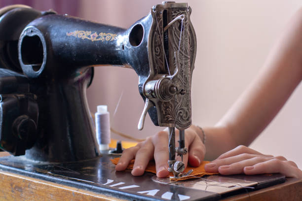 Seamstress sews on an old retro sewing machine. Hands are on the fabric. Close up sewing process. Shallow depth of field. Focus on the hands. Horizontal.