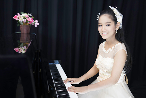 An Asian girl makeup, hair, and wearing a white evening dress for the piano performance.