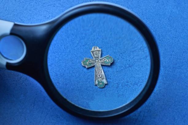 black magnifier enlarges a small old gray silver cross on a blue table