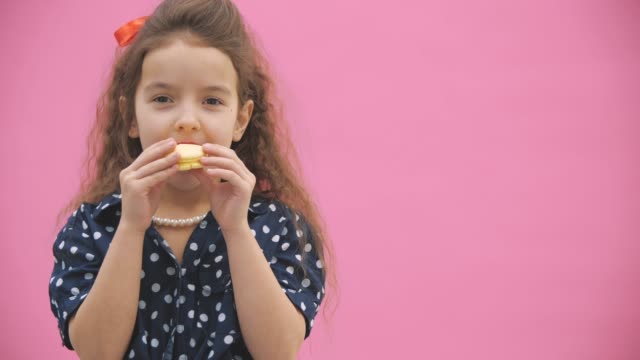 4k close up video where small girl with curly hair eating a yellow macaroon.