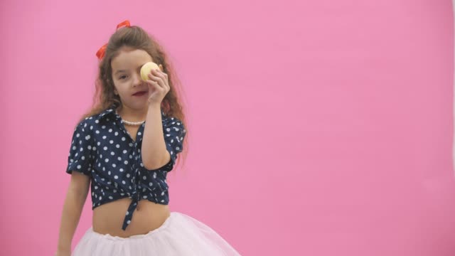 4k video where small girl with curly hair eating a yellow macaroon.