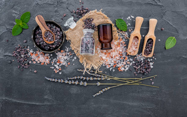 himalaya-schwarzsalz und himalaya-rosa salz mit pfefferminze und lavendel blüte auf dunklem betonhintergrund. himalaya-salz, das häufig beim kochen und für badeprodukte wie badesalze verwendet wird. - alternative medicine herbal medicine aromatherapy oil herb stock-fotos und bilder