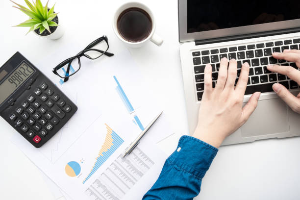 istock Top view of young businessman typing on laptop computer keyboard and analyzing data from the business documents and results of calculation. 1222369291