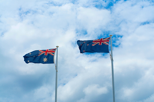 Flags of New Zealand and Australian waving in the wind and against a cloudy blue sky