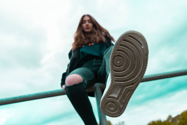 Teenage Girl Stretching Out Sport Shoe Rubber Sole Teenage Girl sitting on fence stretching out her leg, showing the sport shoe rubber sole. Teenage Lifestyle Portrait. Shot from below, Selective Focus on Sport Shoue Rubber Sole. young cool girl stock pictures, royalty-free photos & images