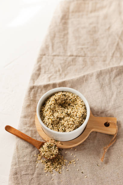 Cannabis kernels in a white bowl with a wooden spoon on a linen napkin on a white table