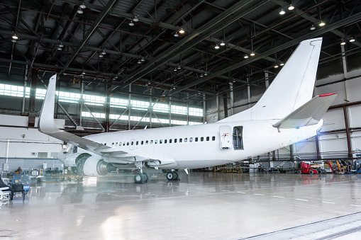 White jet plane in the hangar. Passenger aircraft under maintenance. Checking mechanical systems for flight operations