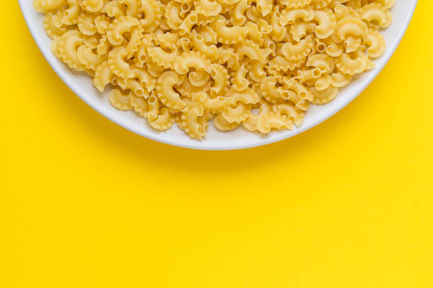 istock many dry unprepared pasta - cockerels on a beige plate on a yellow background, copy space for text 1222373202