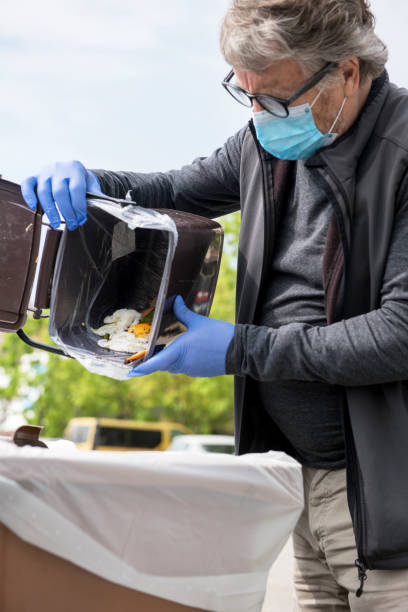 istock Senior Man with Face Mask Throwing Biodegradable Kitchen Waste into a Brown Container in the Coronavirus Time, Europe 1222377162