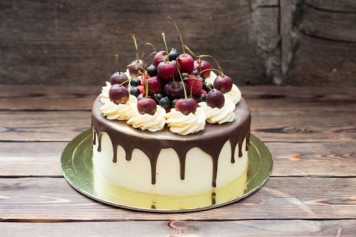 Homemade cake with melted chocolate decorated with whipped cream and fresh cheries on top. Rustic background.