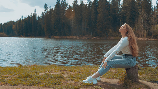 Beautiful young blonde woman sitting and relax in a park near the lake. Side view.