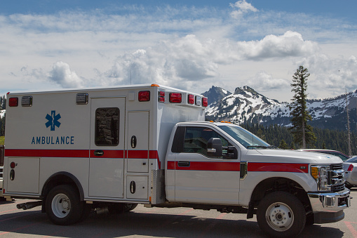 Mount Rainier National Park, State Washington, USA, on the first of july 2019. An ambulance parked in a parking lot, with snowy mountain peaks in the distance.