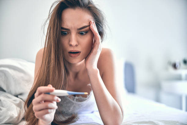 istock Caucasian sick lady looking at thermometer on soft bed 1222384323